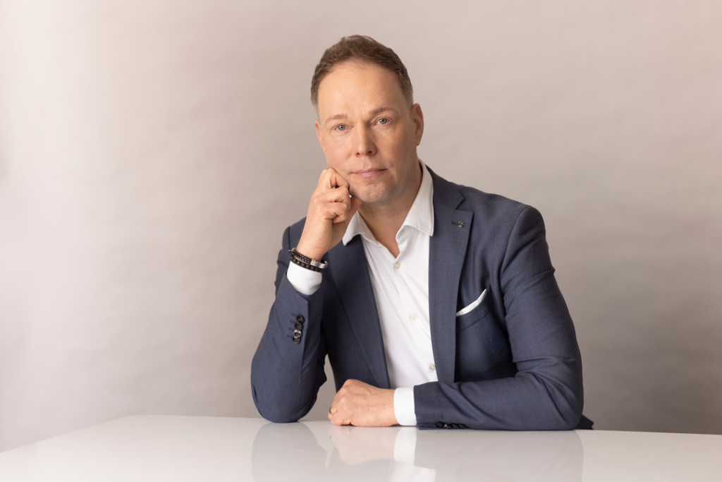 Mies poseeraa pöydän ääressä katsoen kameraan.