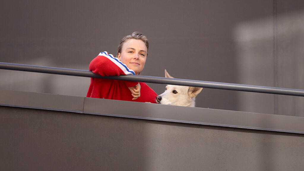 Kiira Korpi koiransa Pikan kanssa. Kaksikko kurkkaa alaspäin kaiteen takaa.