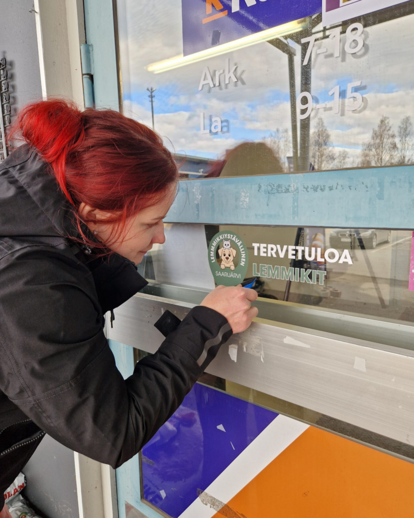 Nainen kiinnittää lemmikit tervetuloa -tarraa kaupan oveen.